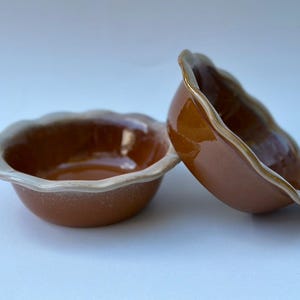 May include: Two brown ceramic bowls with a scalloped edge and a white glaze on the rim. The bowls are stacked on top of each other.