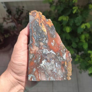 Puede incluir: Una losa grande de ágata pulida de forma irregular con una mezcla de colores rojo, naranja, amarillo, negro y blanco. El ágata tiene un patrón de remolino y capas.