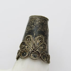 May include: A white horn with a silver cap. The cap has a decorative design of swirls and a scalloped edge.