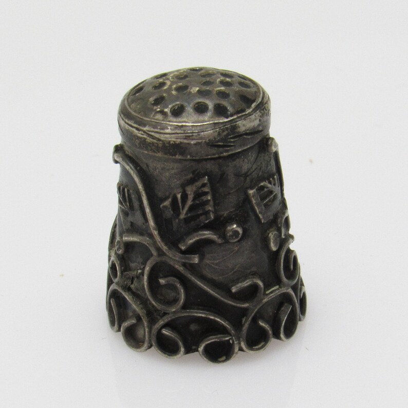 May include: A silver thimble with a decorative floral design and a pierced top.