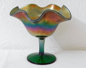 May include: An iridescent glass pedestal bowl with a ruffled rim. The bowl transitions from green to gold and features a floral design on the interior. The base and stem are green.