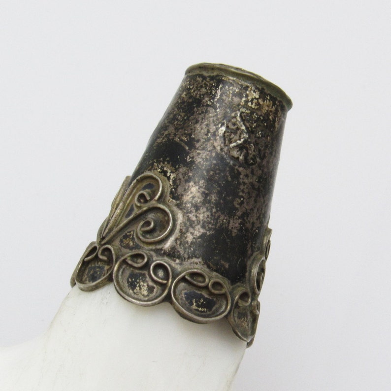 May include: Close-up of a silver bottle stopper with an ornate design. The stopper is made of metal and has a tarnished finish.