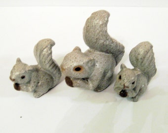 May include: Three gray ceramic squirrel figurines of varying sizes. The squirrels are holding nuts in their paws.
