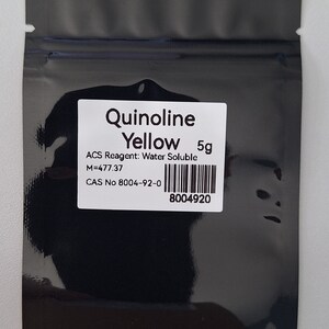 Peut inclure: Un sac refermable noir contenant une étiquette blanche avec le texte "Quinoline Yellow 5g ACS Reagent: Water Soluble M=477.37 CAS No 8004-92-0 8004920"