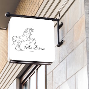 May include: A white sign with a black line drawing of a horse rearing up on its hind legs. The sign says "The Barn" in black cursive lettering.