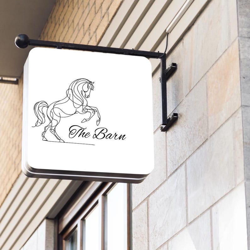 May include: A white sign with a black line drawing of a horse rearing up on its hind legs. The sign says "The Barn" in black cursive lettering.