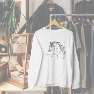 May include: White long-sleeved shirt with a black line drawing of a horse's head on the front.