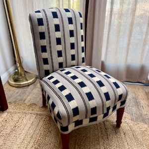 Könnte beinhalten: Gepolsterter Stuhl mit einem Muster aus marineblauen und cremefarbenen Quadraten und bordeauxfarbenen Streifen. Die Beine sind dunkelrot. Der Stuhl steht auf einem gewebten Jute-Teppich.