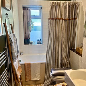 May include: A bathroom interior featuring a white bathtub, a striped shower curtain, and a bamboo towel rack. The shower curtain has vertical black and white stripes with brown accents. A window with a sheer curtain is visible.