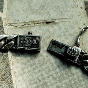 May include: A silver chain bracelet with a clasp featuring a snake design and the letters "L.S.A."