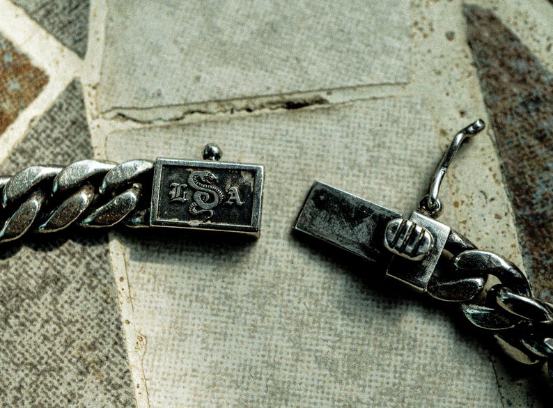 May include: A silver chain bracelet with a clasp featuring a snake design and the letters "L.S.A."