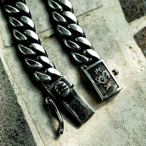 May include: A silver curb chain bracelet with a clasp featuring a dragon design and the text "E.S.A."