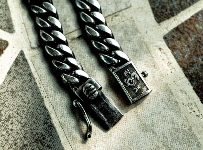 May include: A silver curb chain bracelet with a clasp featuring a dragon design and the text "E.S.A."