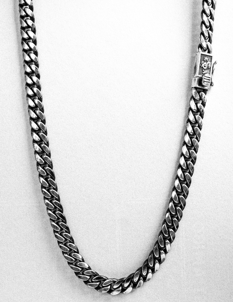 May include: A silver curb chain necklace with a clasp.