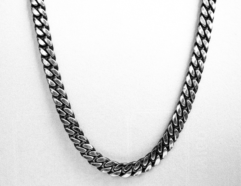 May include: A silver curb chain necklace with a thick, textured design.
