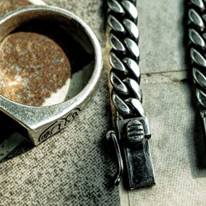 May include: A silver ring with an intricate design and a silver chain bracelet with a clasp that has a snake design. The bracelet has the text "The Serpent" on the clasp.
