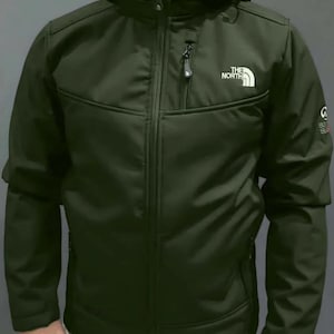 May include: Olive green hooded jacket with a full-length zipper and the white "THE NORTH FACE" logo on the chest. The jacket has a small zippered chest pocket and a small logo on the sleeve.