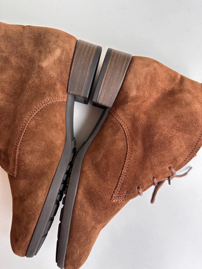 K&ouml;nnte beinhalten: Ein Paar braune Wildlederstiefel mit niedrigem Absatz. Die Stiefel haben ein Schn&uuml;rdesign und eine strukturierte Sohle. Die Farbe ist ein warmes, erdiges Braun, und die Stiefel scheinen ungetragen zu sein.
