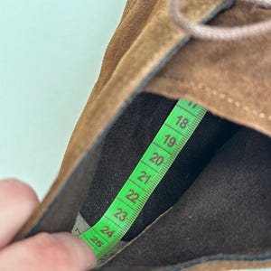 K&ouml;nnte beinhalten: Nahaufnahme eines braunen Wildlederschuhs mit Schn&uuml;rsenkeln. Ein gr&uuml;nes Ma&szlig;band zeigt die Innenl&auml;nge des Schuhs, ca. 23 cm. Die Innenseite des Schuhs ist dunkelbraun, die Au&szlig;enseite hellbraun.