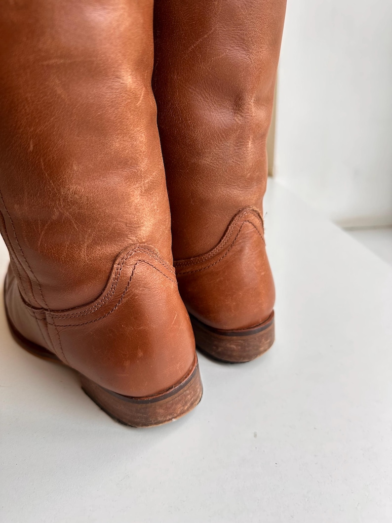 Pu&ograve; includere: Primo piano di due stivali in pelle marrone. Gli stivali presentano segni di usura con pieghe e leggera scoloritura. Le suole sono marrone scuro, che mostrano usura. Gli stivali sembrano essere vintage o ben usati.