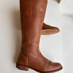 Pu&ograve; includere: Un paio di stivali alti in pelle marrone. Gli stivali hanno un design classico con punta arrotondata e tacco basso. La pelle ha una tonalit&agrave; ricca e calda. Gli stivali sono alti circa 40 cm.