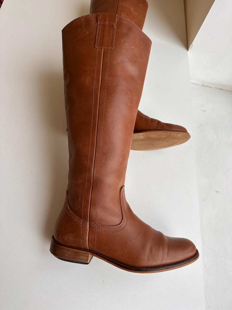 Pu&ograve; includere: Un paio di stivali alti in pelle marrone. Gli stivali hanno un design classico con punta arrotondata e tacco basso. La pelle ha una tonalit&agrave; ricca e calda. Gli stivali sono alti circa 40 cm.