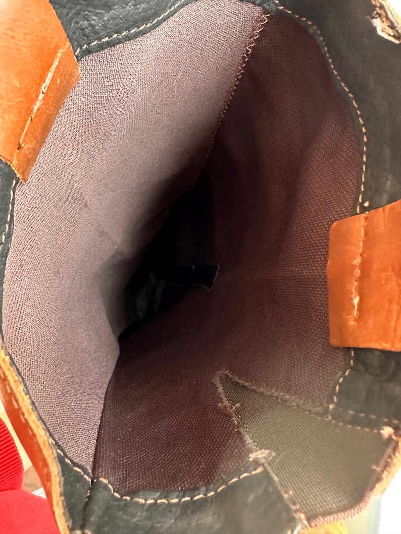 Pu&ograve; includere: Vista ravvicinata all'interno di uno stivale alto. Lo stivale presenta una combinazione di pelle marrone, nera e arancione. La fodera interna &egrave; in tessuto marrone tenue. Le cuciture bianche accentuano le cuciture.
