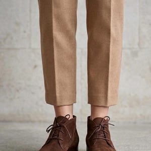 K&ouml;nnte beinhalten: Braune Wildleder-Ankle Boots mit Schn&uuml;rsenkeln, kombiniert mit beigefarbenen Hosen. Die Stiefel haben einen kleinen Absatz und ein klassisches Design, passend f&uuml;r den Alltag. Die Hose ist in einer neutralen Farbe gehalten.