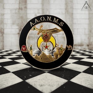 May include: A gold-colored Masonic emblem with the letters "A.A.O.N.M.S." around the perimeter. The emblem features a crescent moon, a five-pointed star, a sword, and a pyramid.