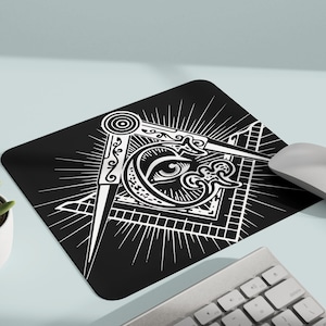 May include: Black and white mouse mat featuring a Masonic symbol, with a compass and square, an all-seeing eye, and a radiating starburst design.