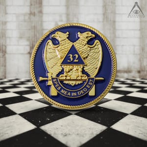 May include: A gold-colored Masonic pin with a blue enamel background. The pin features a double-headed eagle with outstretched wings, a triangle with the number 32 inside, and the text "Spes Mea In Deo Est".