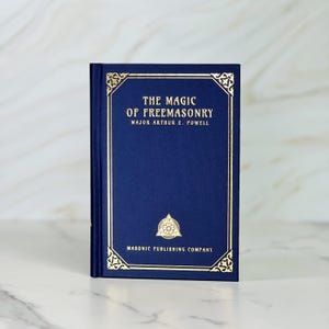 May include: A navy blue hardback book with gold lettering and a gold border. The title is "The Magic of Freemasonry" by Major Arthur E. Powell. The book is published by Masonic Publishing Company.