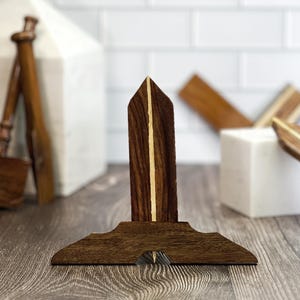 May include: A wooden drafting tool with a pointed tip and a base shaped like a triangle. The tool is made of dark wood with light wood accents.