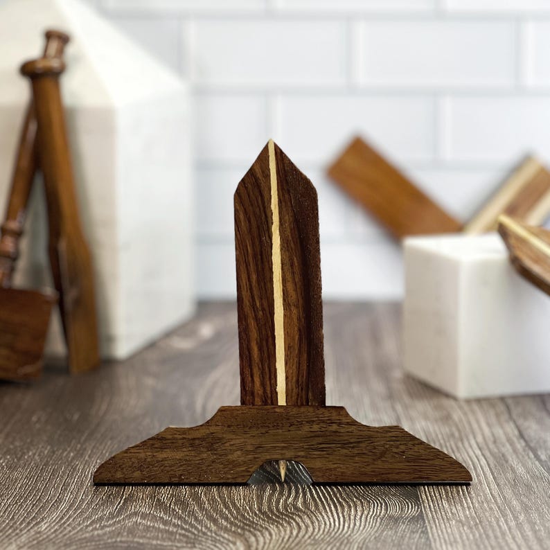 May include: A wooden drafting tool with a pointed tip and a base shaped like a triangle. The tool is made of dark wood with light wood accents.