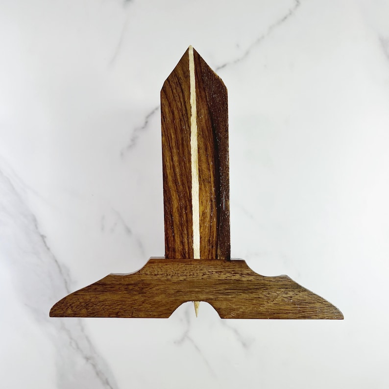 May include: A wooden T-ruler with a white inlay down the center of the vertical piece. The ruler has a pointed tip at the bottom.