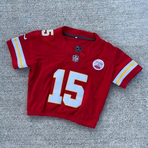 Peut inclure: Un maillot de football rouge avec le num&eacute;ro 15 en blanc sur le devant et le num&eacute;ro 5 sur l'&eacute;paule. Le maillot a des rayures jaunes et blanches sur les manches et le logo NFL.