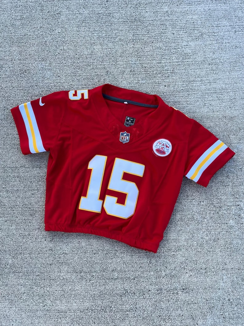 Peut inclure: Un maillot de football rouge avec le num&eacute;ro 15 en blanc sur le devant et le num&eacute;ro 5 sur l'&eacute;paule. Le maillot a des rayures jaunes et blanches sur les manches et le logo NFL.