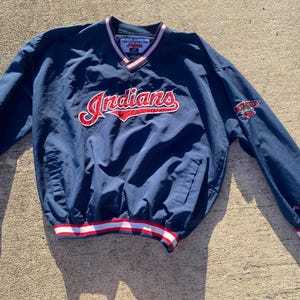 Könnte beinhalten: Eine marineblaue Langarm-Pulloverjacke mit V-Ausschnitt und rot-weißen Streifen. Das Wort Indians ist in Rot und Weiß auf die Brust gestickt. Ein kleines Teamlogo befindet sich auf dem linken Ärmel und die Ärmelbündchen sind rot-weiß gestreift.