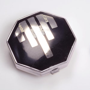 May include: A silver octagonal compact with a black enamel top and a geometric design in silver and white.