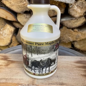 May include: A white plastic bottle of Vermont Pure Maple Syrup with a brown cap. The bottle has a winter scene with a horse-drawn sleigh on the front. The label reads "Vermont Pure Maple Syrup" and "32 FL OZ".