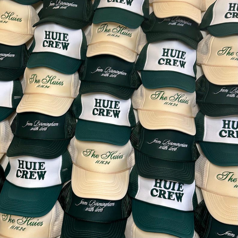 May include: A stack of green and beige trucker hats with the text "The Huies 11/16/94" and "Huie Crew" embroidered on them. The hats have a mesh back and a white front panel.