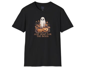 May include: Black t-shirt featuring a Halloween-themed graphic. The design includes a white ghost, two carved pumpkins, and floral elements. The text "JUST HERE FOR THE BOOS" is printed below the pumpkins.