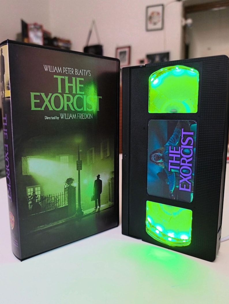 May include: A black VHS tape with the movie title "The Exorcist" and a matching DVD case. The VHS tape has a green glowing light. The DVD case features a dark green and black movie poster.