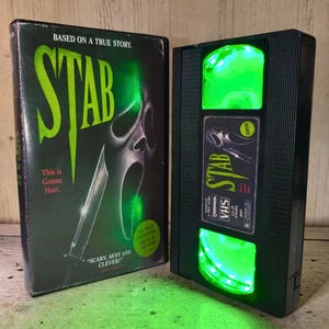 Puede incluir: Una cinta VHS negra y su estuche a juego titulado Stab. El estuche presenta una máscara de fantasma teñida de verde y un cuchillo con el texto Based on a True Story, This is Gonna Hurt y Scary, Sexy and Clever. La cinta tiene luces verdes brillantes.