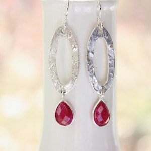 May include: Silver dangle earrings with a hammered oval design and a teardrop-shaped red gemstone.