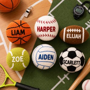May include: Six crocheted sports balls featuring the names Liam, Harper, Elijah, Zoe, Aiden, and Scarlett. The collection includes a basketball, baseball, football, tennis ball, volleyball, and soccer ball, accompanied by a whistle and stopwatch.