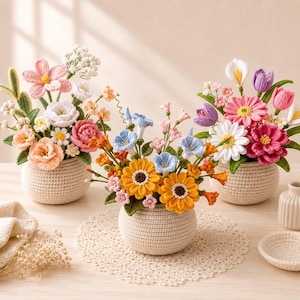 May include: Three crochet flower arrangements in round, cream-colored crocheted pots. The bouquets feature a variety of colorful handmade flowers including pink, orange, yellow, blue, and white blossoms with green leaves, displayed on a lace doily.