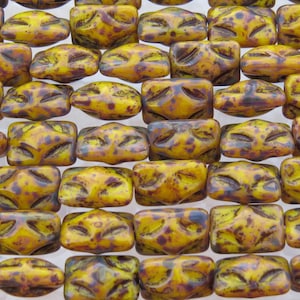 May include: A close-up of a collection of yellow and brown glass beads with a textured surface. The beads are rectangular in shape and have a mottled appearance.