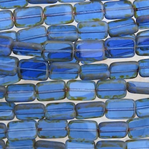May include: Rows of rectangular blue glass beads with a distressed, aged appearance. The beads have a lighter blue center and darker blue edges with a hint of green. These beads are strung together, perfect for jewelry making.