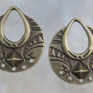 May include: Two antique gold-toned metal earring charms with a decorative design featuring a diamond shape in the center and a teardrop-shaped opening at the top.